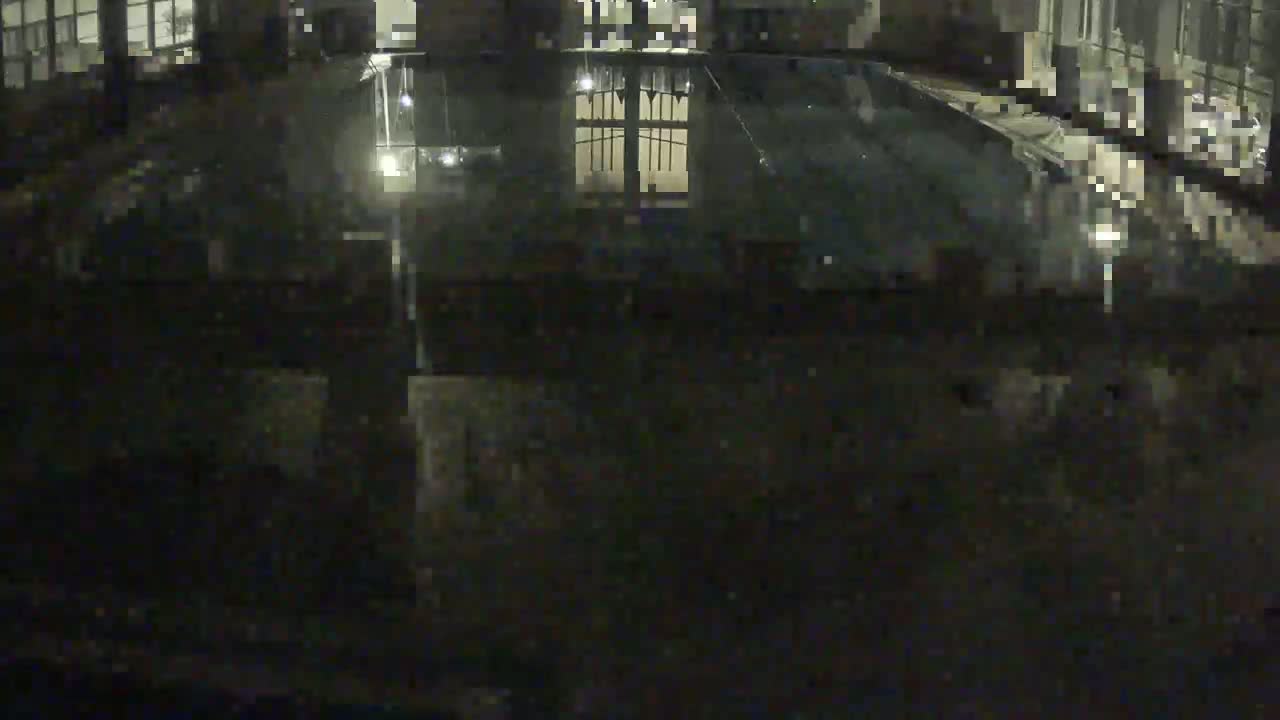 A nighttime, blurry view of a dark, possibly wet, outdoor area with a reflective pool of water and a building in the background.