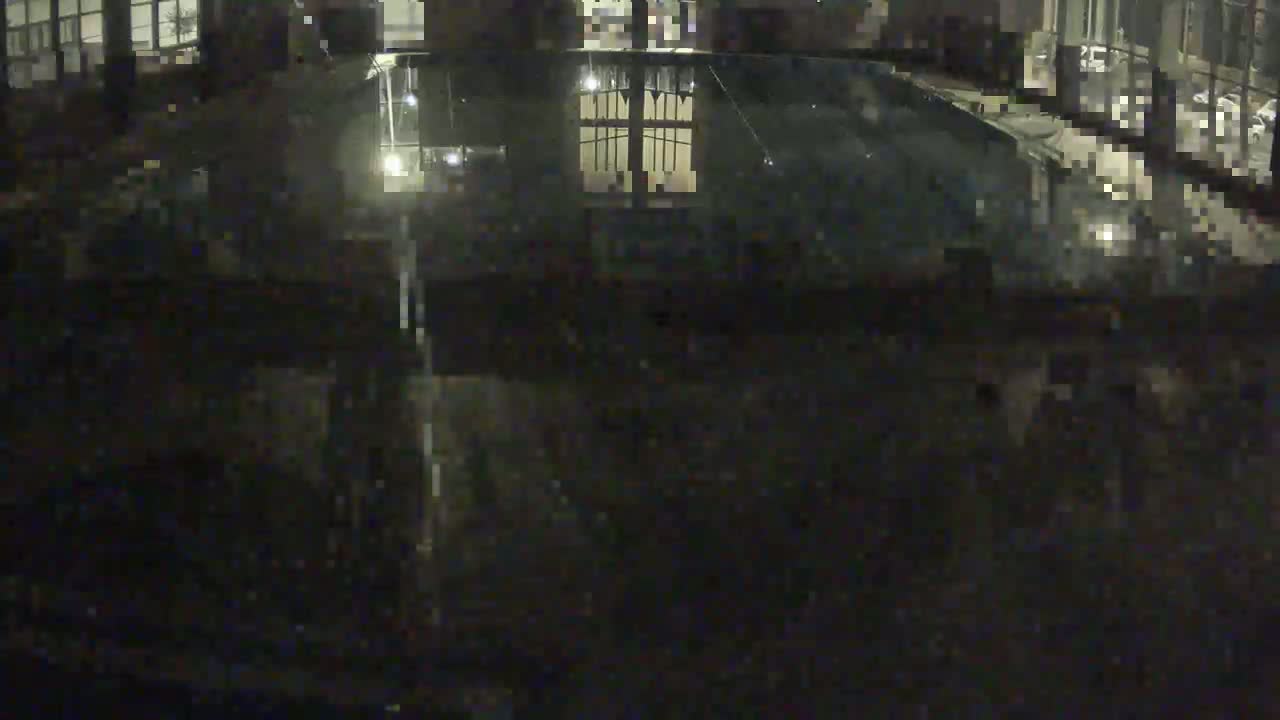 A dark, nighttime view of a mostly empty indoor swimming pool reflecting light from nearby windows.