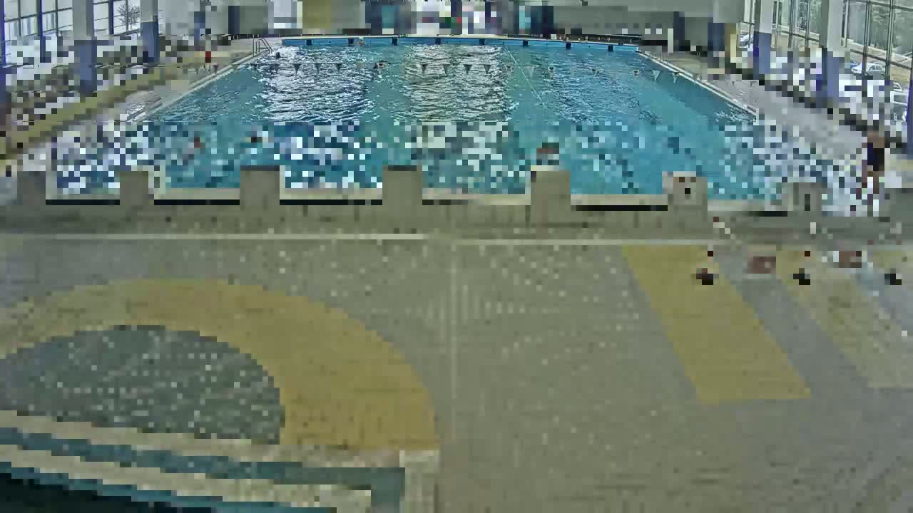 An indoor swimming pool with several people swimming and others sitting on the pool deck.
