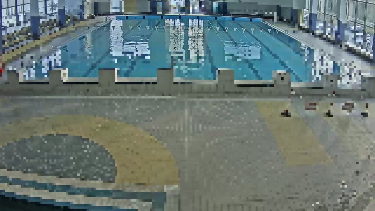 An indoor swimming pool with multiple lanes is seen from an elevated view, surrounded by a tiled deck area.
