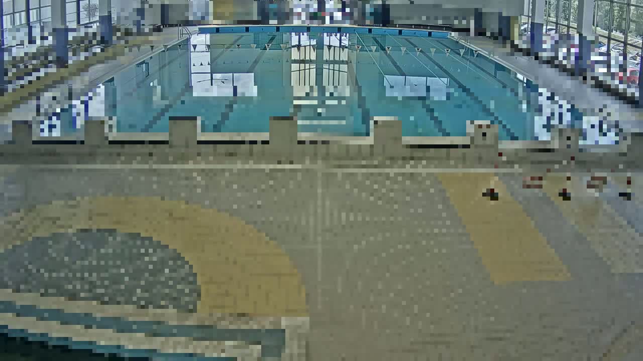 An indoor swimming pool with multiple lanes is seen from an elevated perspective, the surrounding area appearing mostly empty.