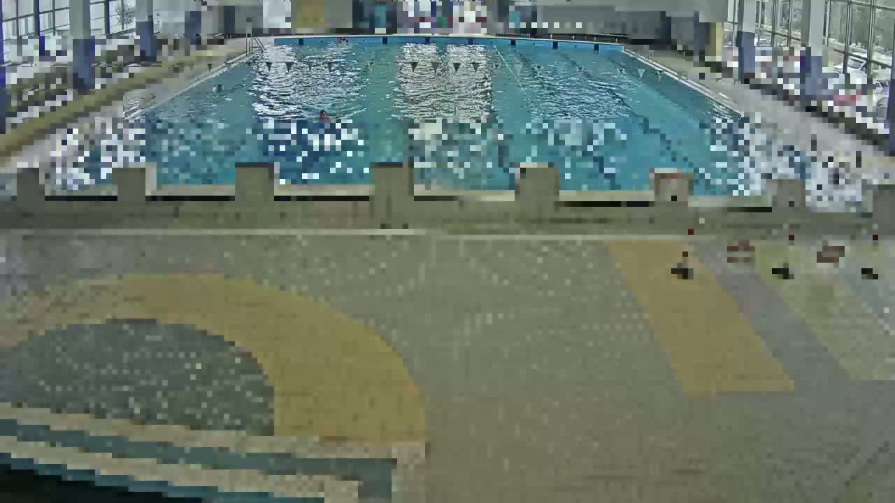 An indoor swimming pool with several people swimming laps, viewed from above.