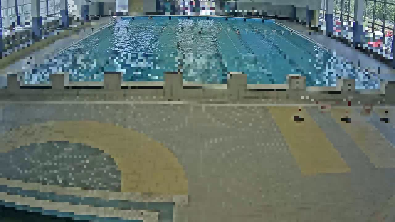 An indoor swimming pool with several people swimming laps and others sitting around the pool deck.