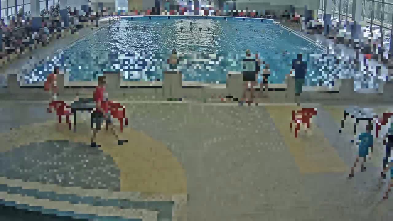 An indoor swimming pool with many people around it, some in the water and others sitting or standing on the pool deck.