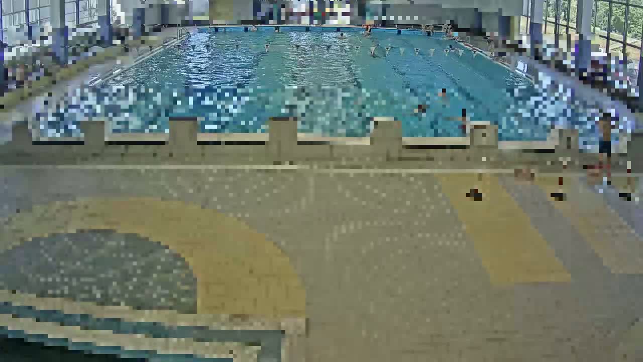 An indoor swimming pool with many people swimming and some people sitting on the pool deck.