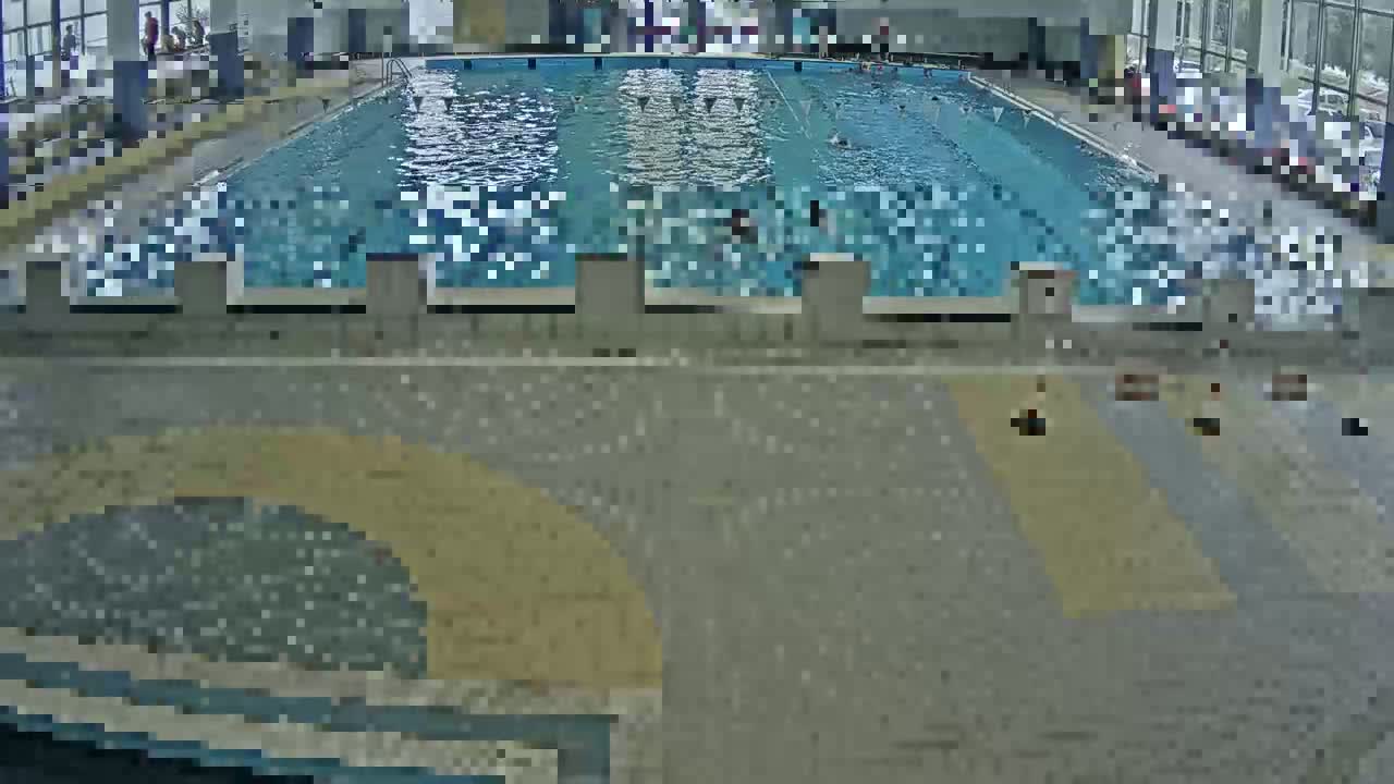 An indoor swimming pool with several people swimming and a few people sitting on the pool deck.