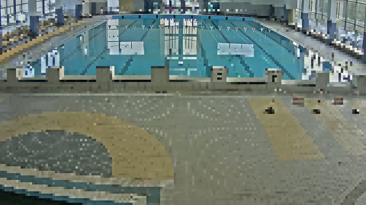 An indoor swimming pool with light-colored tiled flooring and an empty, blue swimming pool.