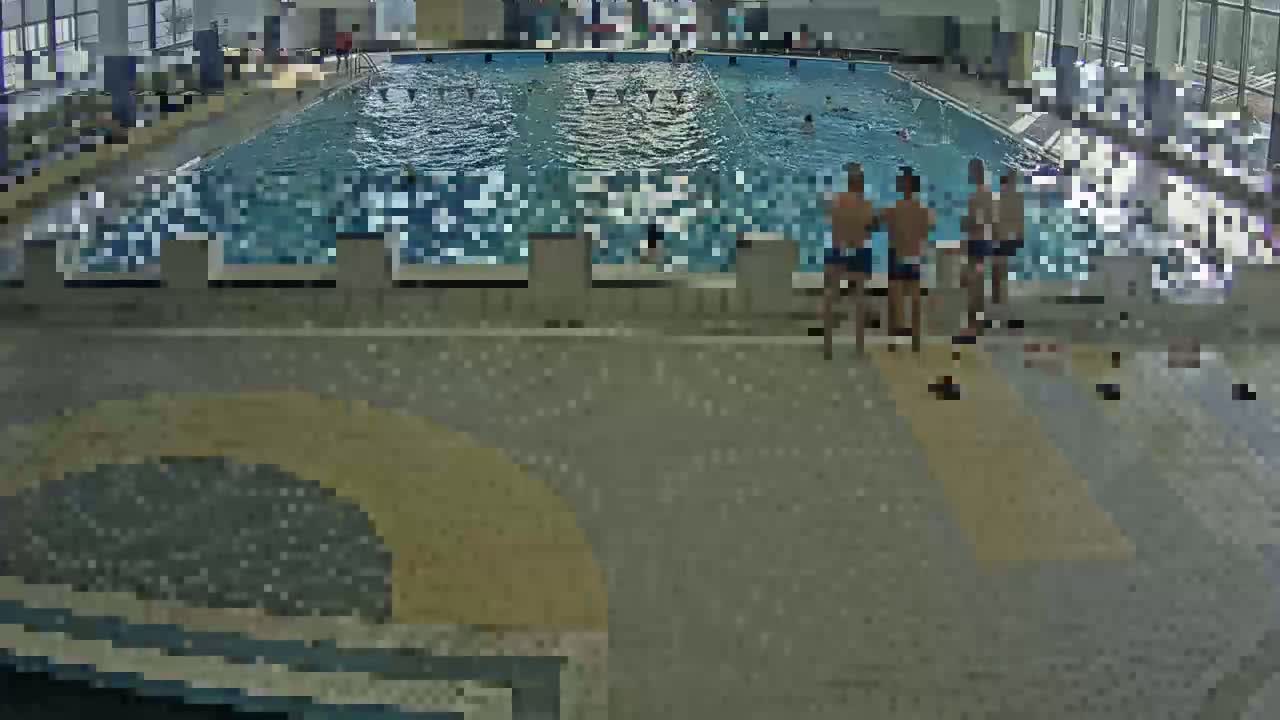 An indoor swimming pool with several people swimming and a few people standing on the pool deck.