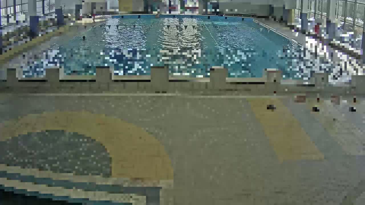 An indoor swimming pool with several people around its edge and a few people swimming in it.