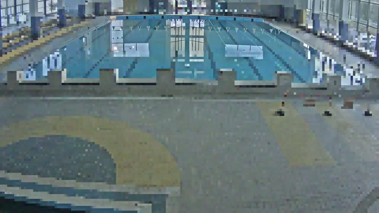An indoor swimming pool with a light-grey tiled floor and several lane dividers is seen from an elevated vantage point.