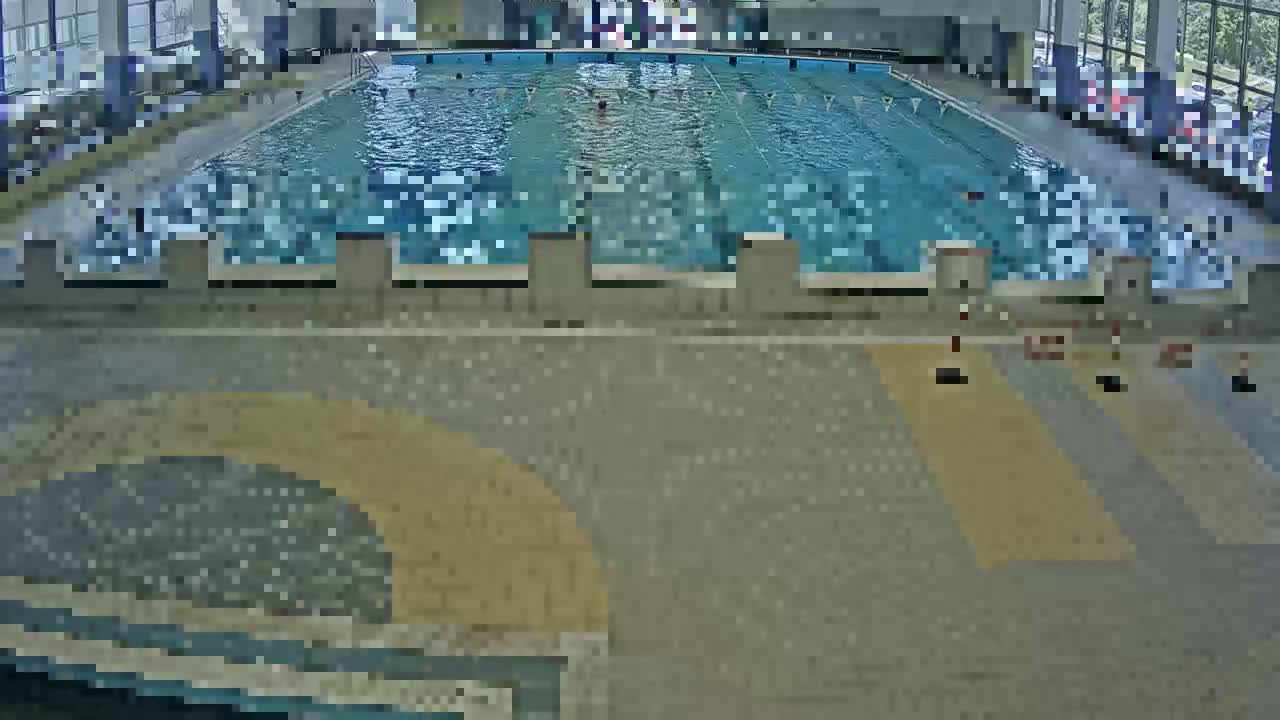 An indoor swimming pool with a light-grey tiled floor and several lane dividers is seen from an elevated vantage point.