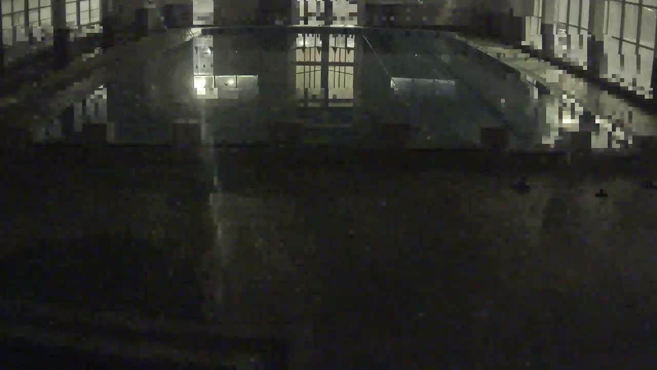 The image shows a dimly lit indoor swimming pool with reflections of interior lights and windows visible on the water and surrounding wet surfaces.
