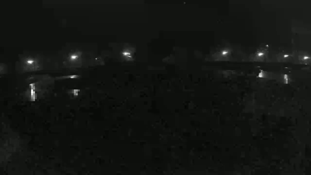 A dark, foggy nighttime scene shows a long row of distant lights reflecting on a body of water.