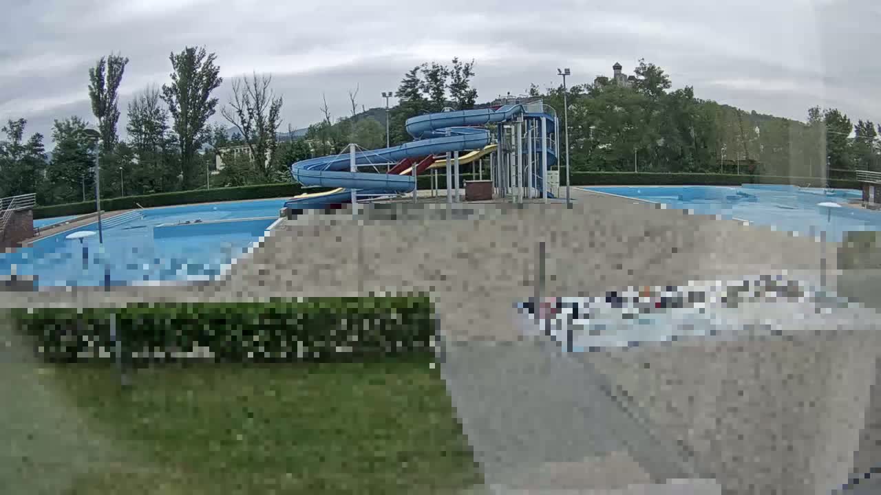 An outdoor swimming pool complex with multiple pools and water slides is visible under an overcast sky.