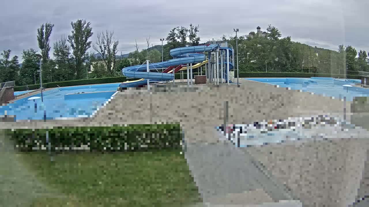 An outdoor swimming pool complex with multiple pools and water slides under an overcast sky.