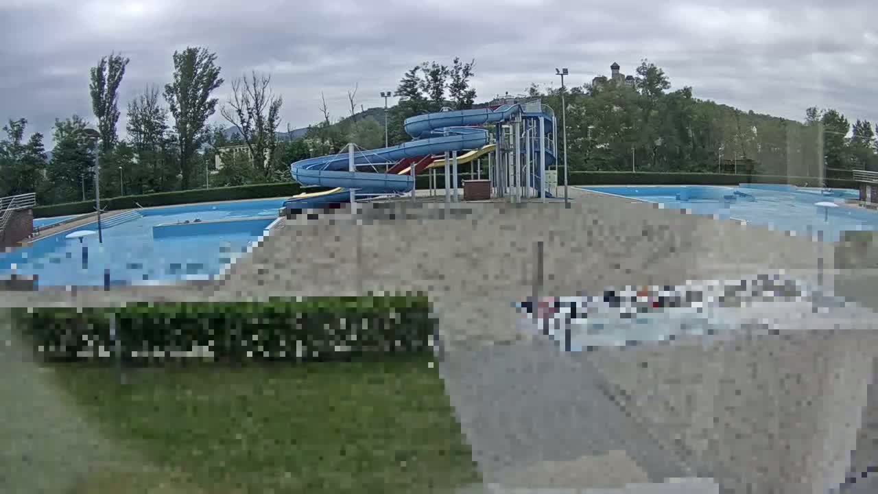 An outdoor swimming pool complex with multiple pools and water slides is visible under an overcast sky.