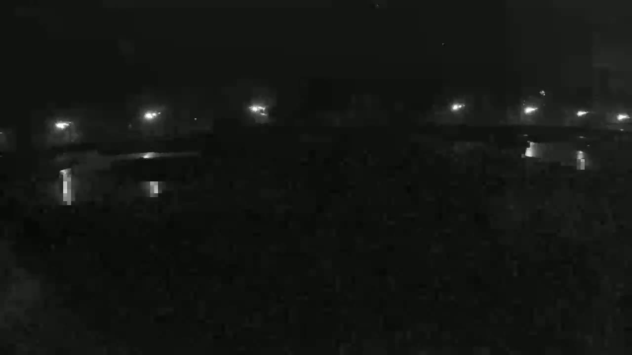 A dark, nighttime scene shows a row of distant lights illuminating a mostly obscured area, possibly a parking lot or field.