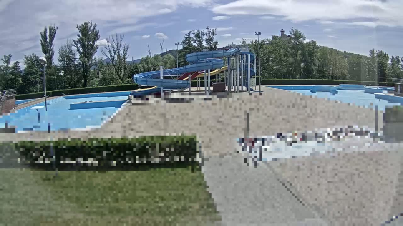 An outdoor swimming pool complex with multiple pools and water slides is visible under a partly cloudy sky.