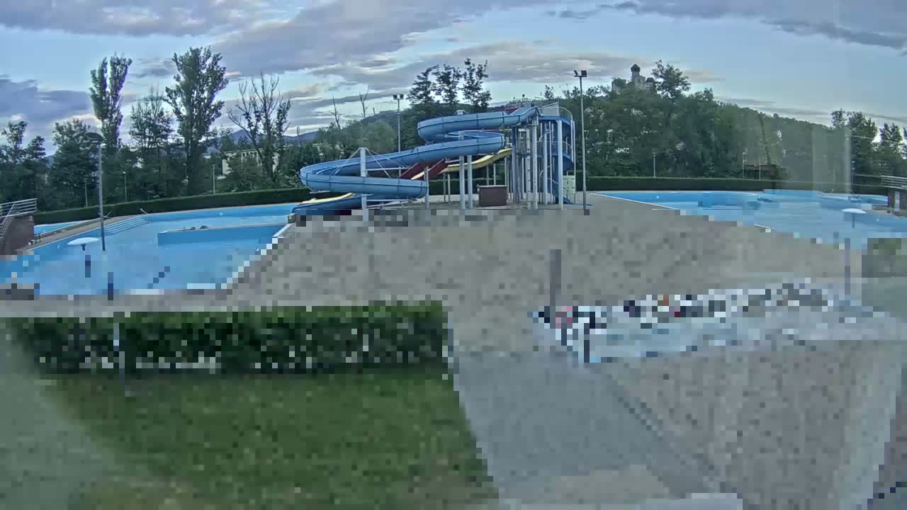 An outdoor swimming pool complex with multiple pools and water slides under a partly cloudy sky.