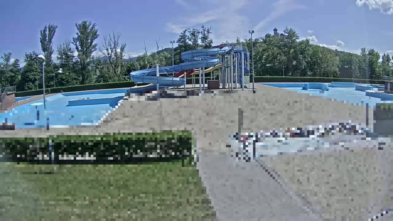 An outdoor swimming pool complex with water slides is visible under a sunny sky.
