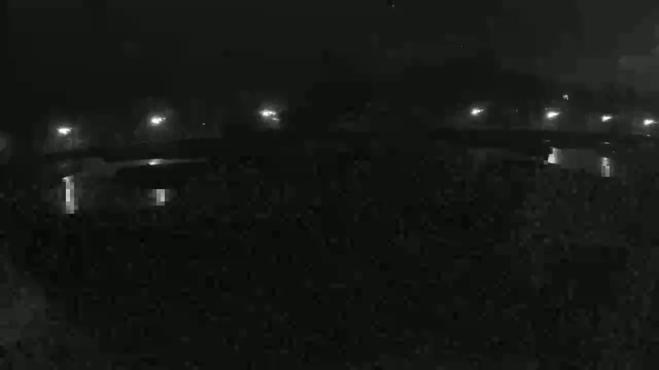 A nighttime, dimly lit scene shows a dark body of water reflecting several distant lights.