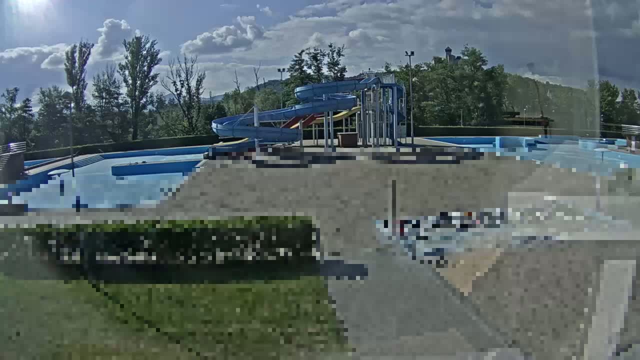 A swimming pool complex with two water slides is visible under a partly cloudy sky.