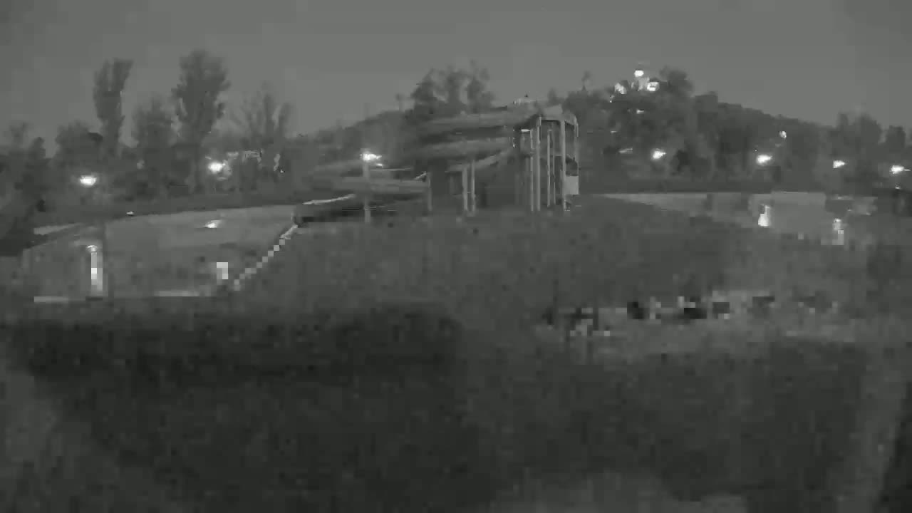 A nighttime, low-light image shows a water park with slides and pools, surrounded by trees and dimly lit.