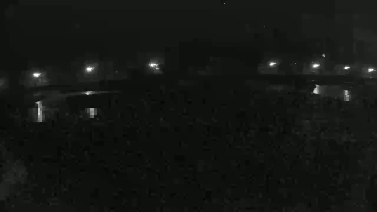 A nighttime, low-light view shows a dark, possibly foggy or hazy, area with dimly lit structures and distant lights.