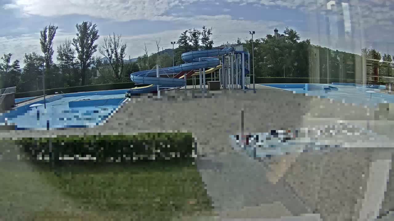 An outdoor swimming pool complex with two twisting water slides is visible under a partly cloudy sky.