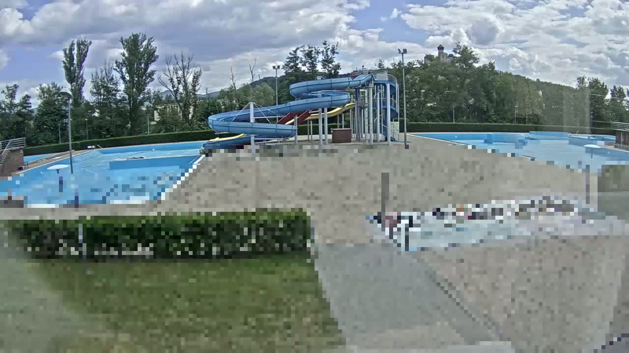A swimming pool complex with multiple pools and water slides is situated outdoors under a partly cloudy sky.
