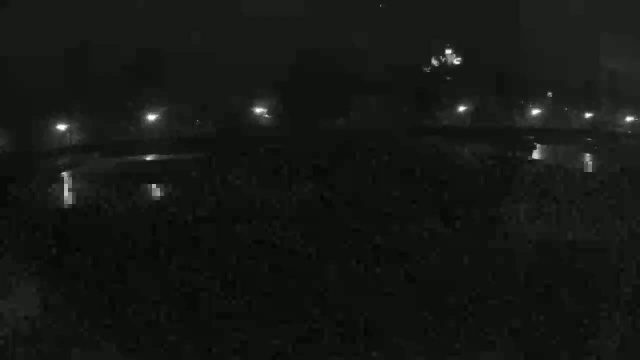 A dark, nighttime scene shows a body of water reflecting the lights of a structure in the distance under a clear, dark sky.
