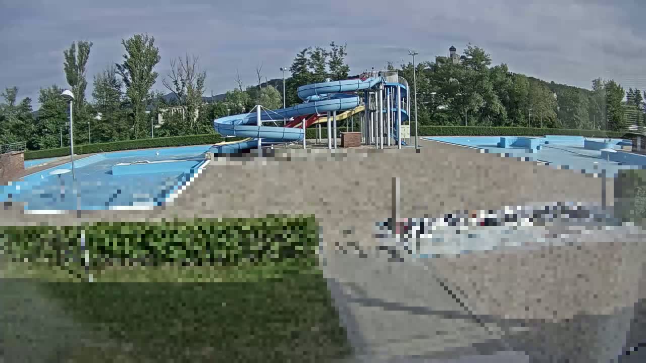 An outdoor swimming pool complex with two spiral water slides is visible under a mostly sunny sky.