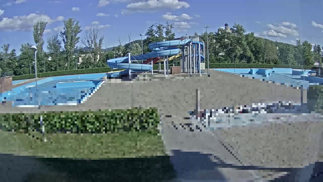 A swimming pool complex with multiple pools and twisty water slides is visible on a sunny day.