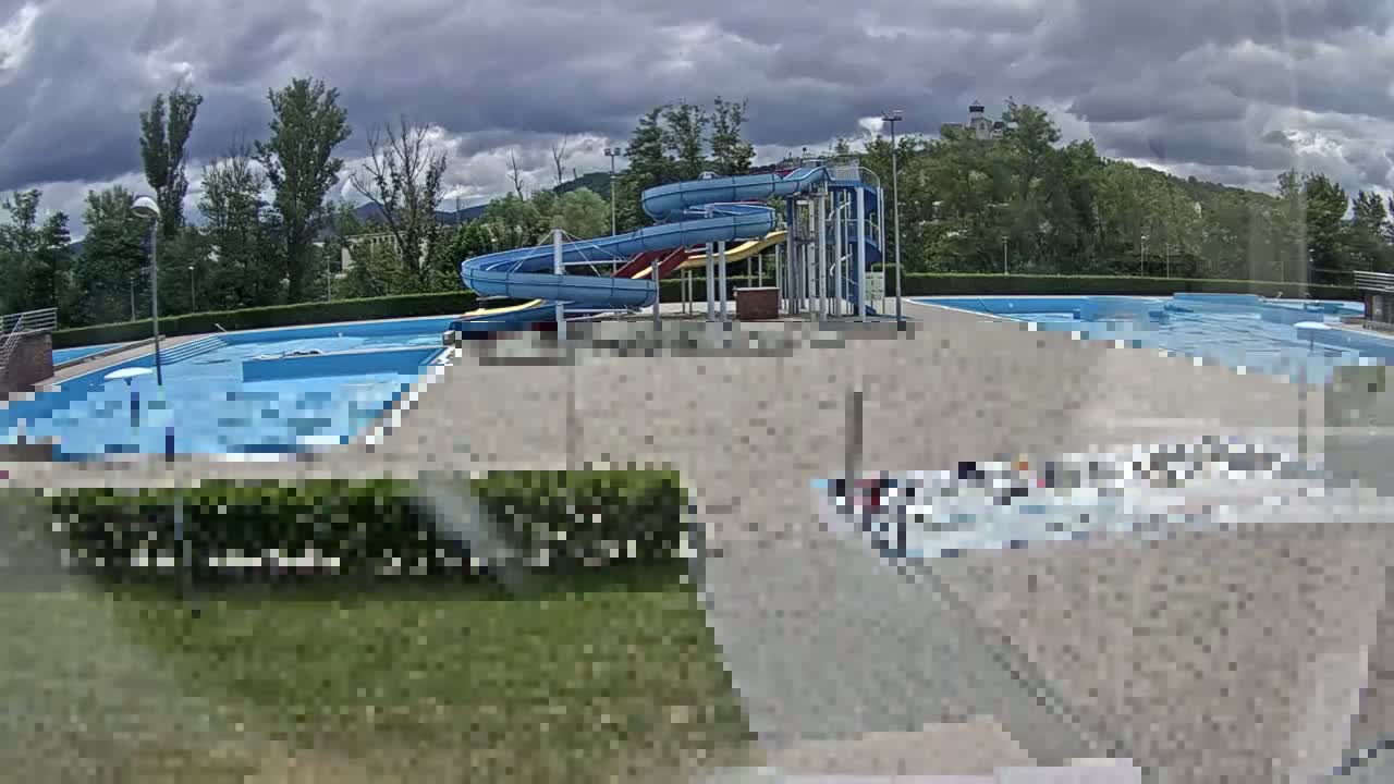 An outdoor swimming pool complex with water slides sits under a cloudy sky.