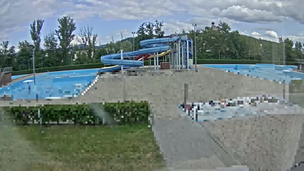 An outdoor swimming pool complex with water slides is visible under a partly cloudy sky.