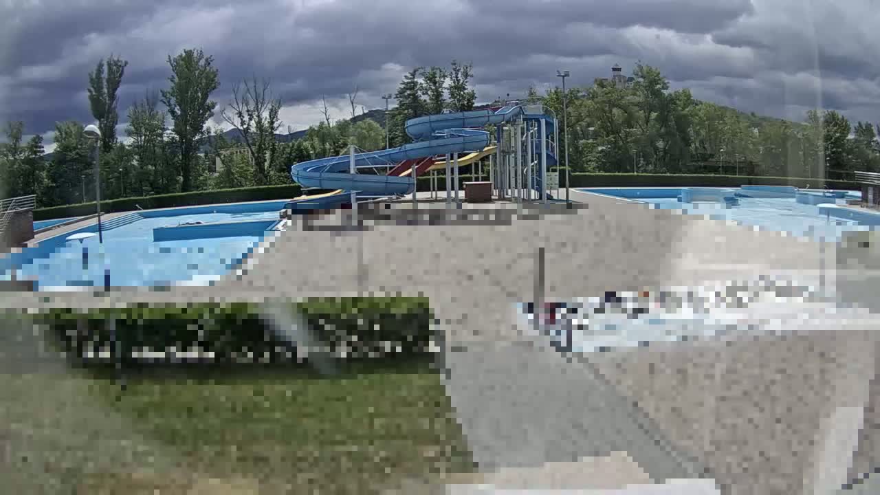 An outdoor swimming pool complex with water slides sits under a partly cloudy sky.
