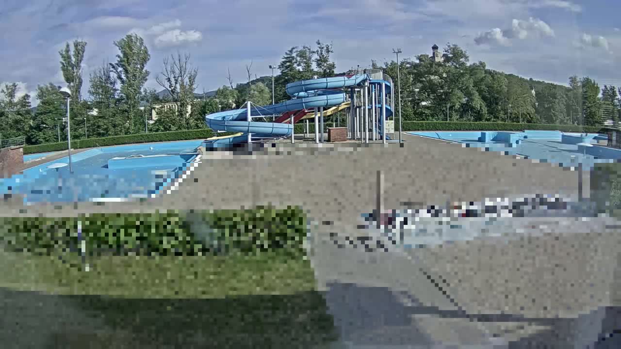 An outdoor swimming pool with two spiral water slides is visible under a partly cloudy sky.