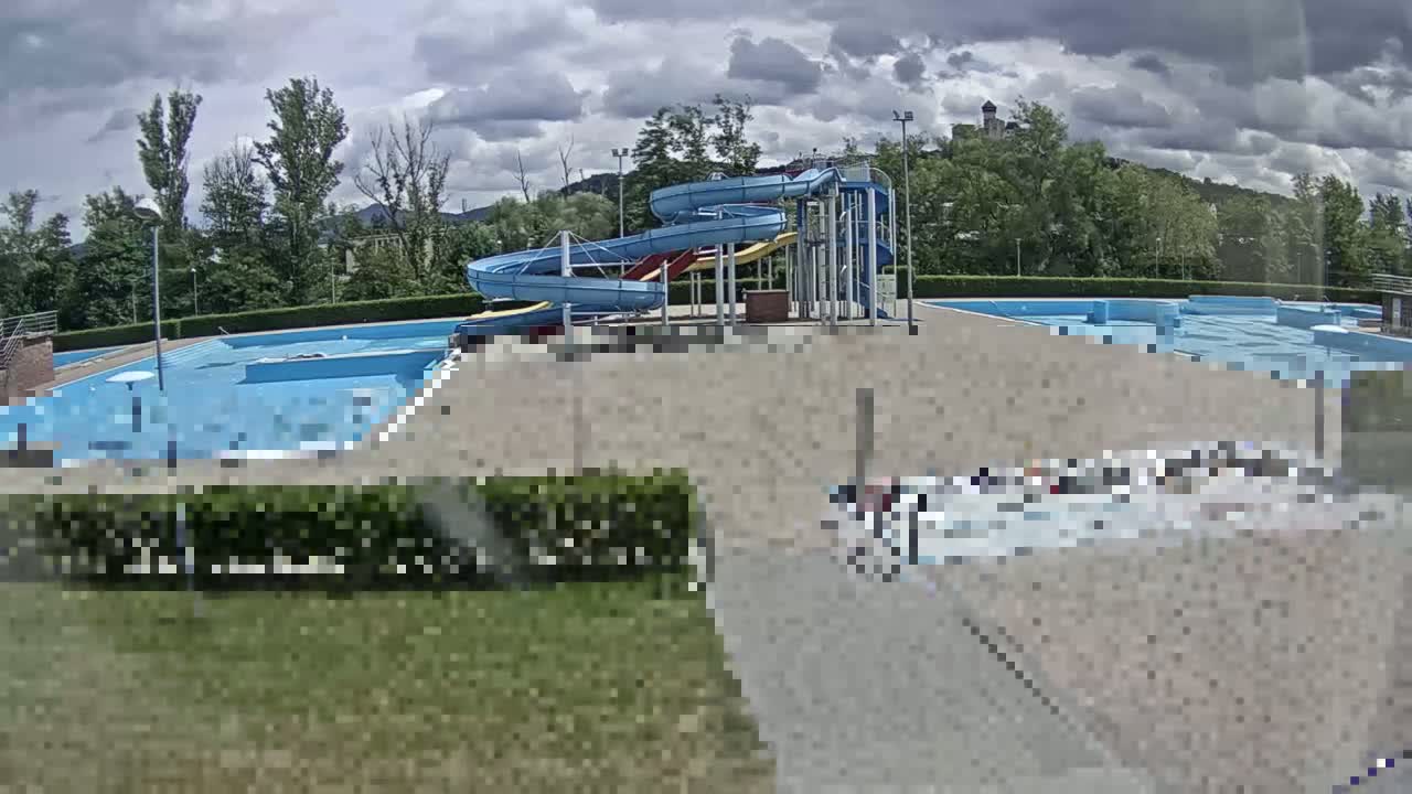 An outdoor swimming pool complex with two winding water slides is visible under a partly cloudy sky.