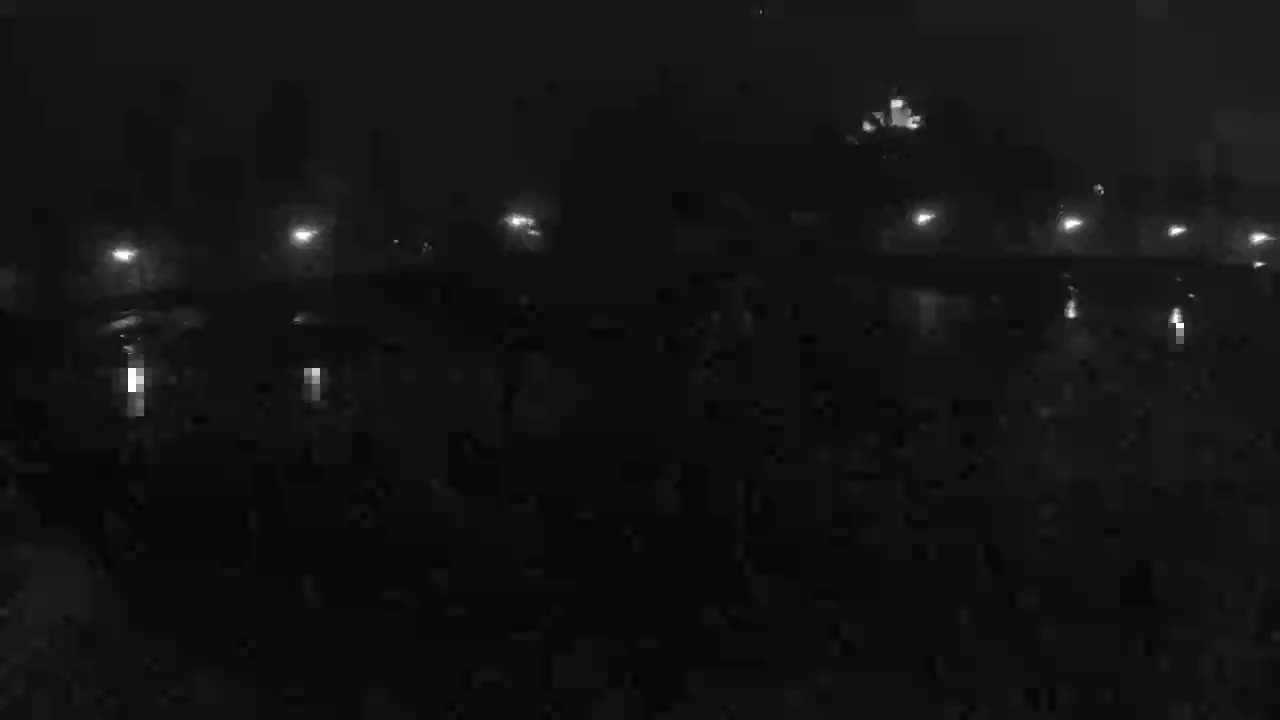 A nighttime view of a bridge with lights illuminating a dark, possibly foggy or hazy, body of water.