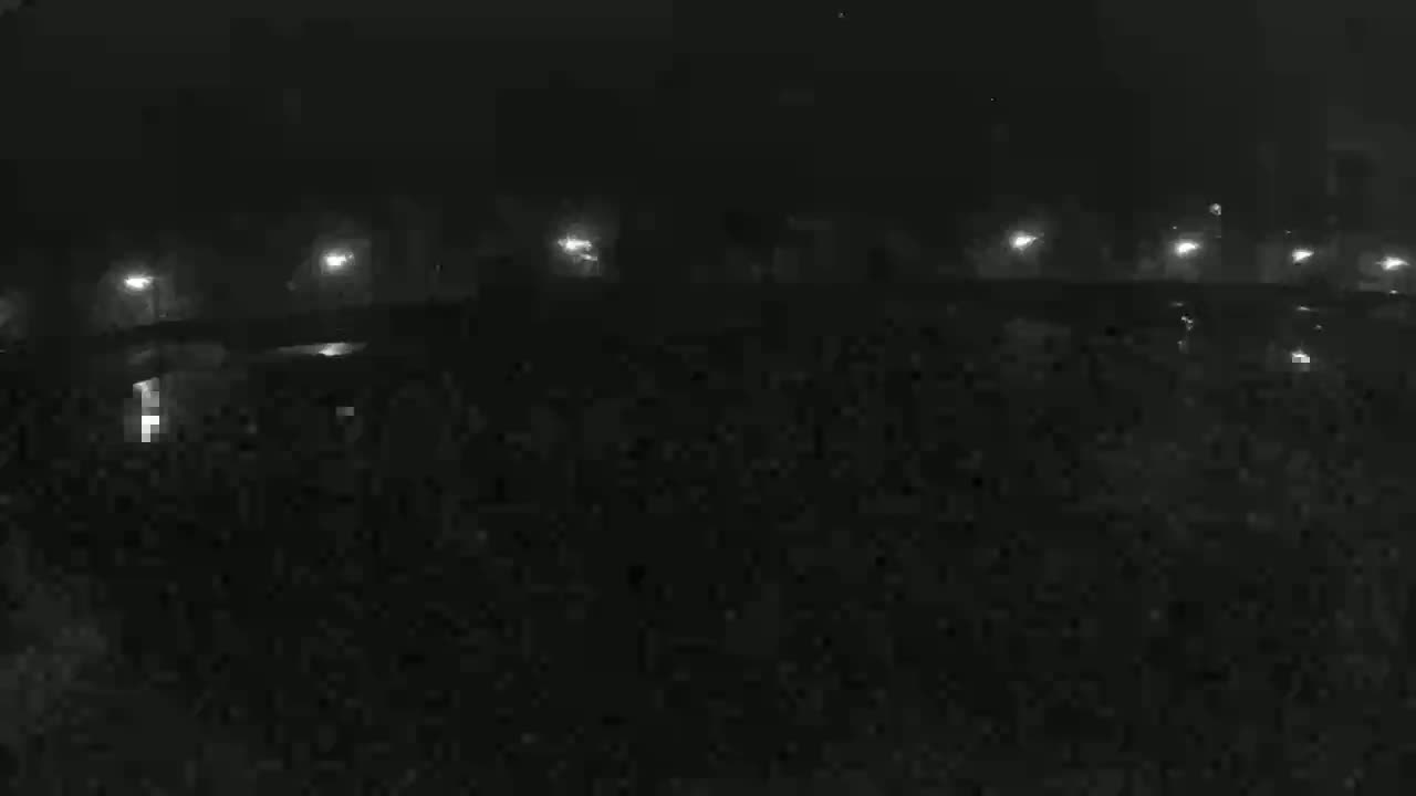 A nighttime view shows dimly lit structures and possibly vehicles under a foggy or hazy sky.
