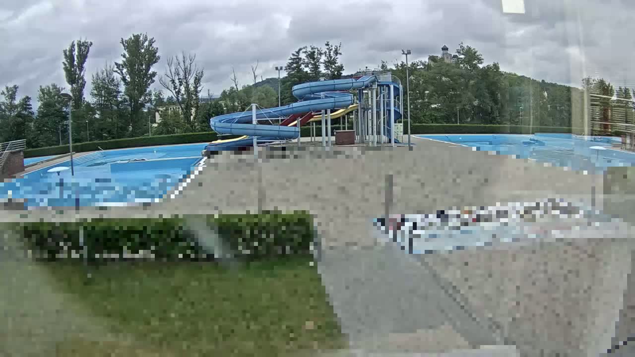 An outdoor swimming pool complex with a double water slide is seen under an overcast sky.