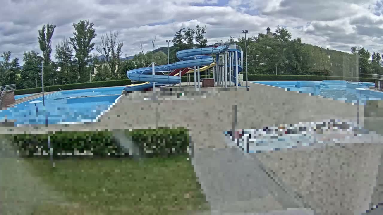 An outdoor swimming pool complex with multiple pools and a water slide is visible under a partly cloudy sky.