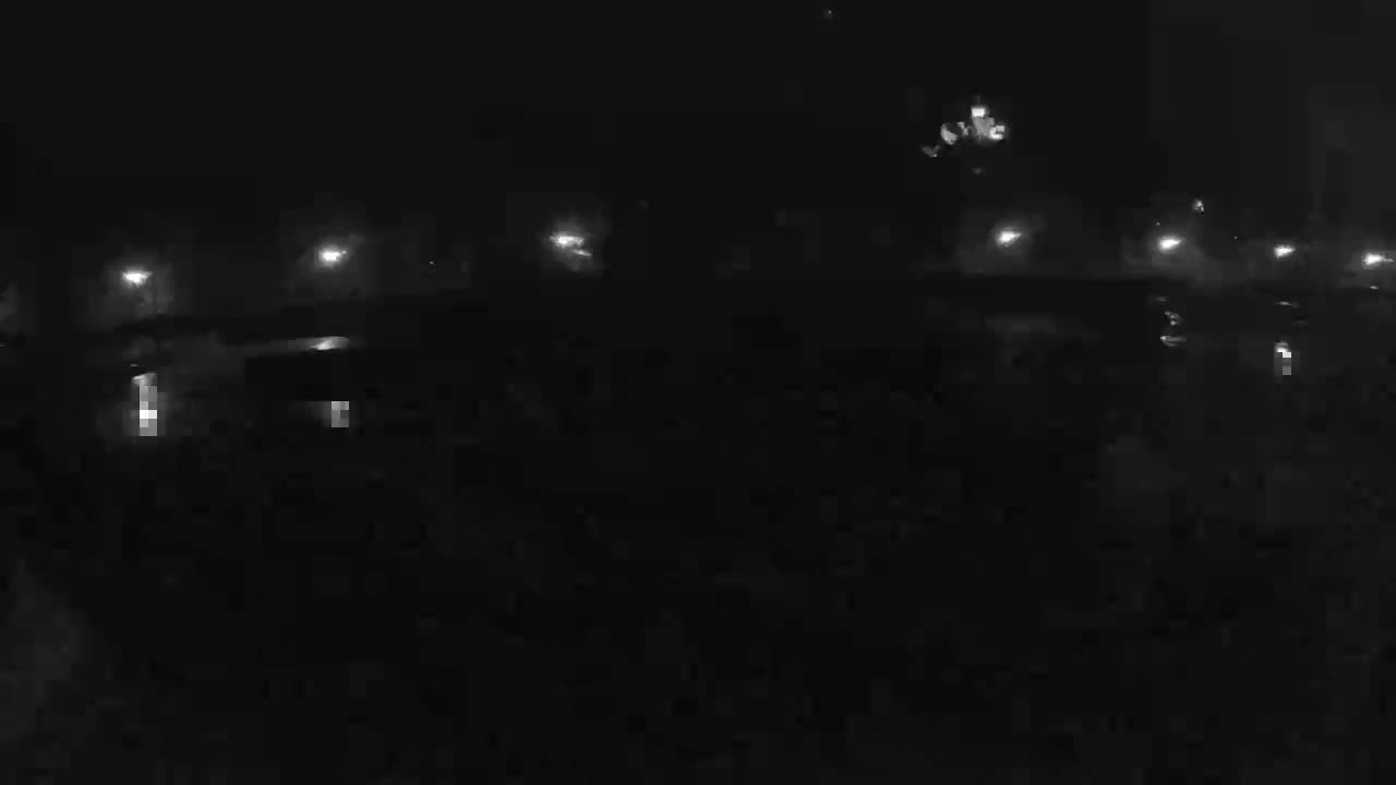 A dark, nighttime scene shows dimly lit cars parked in a lot under a hazy sky.