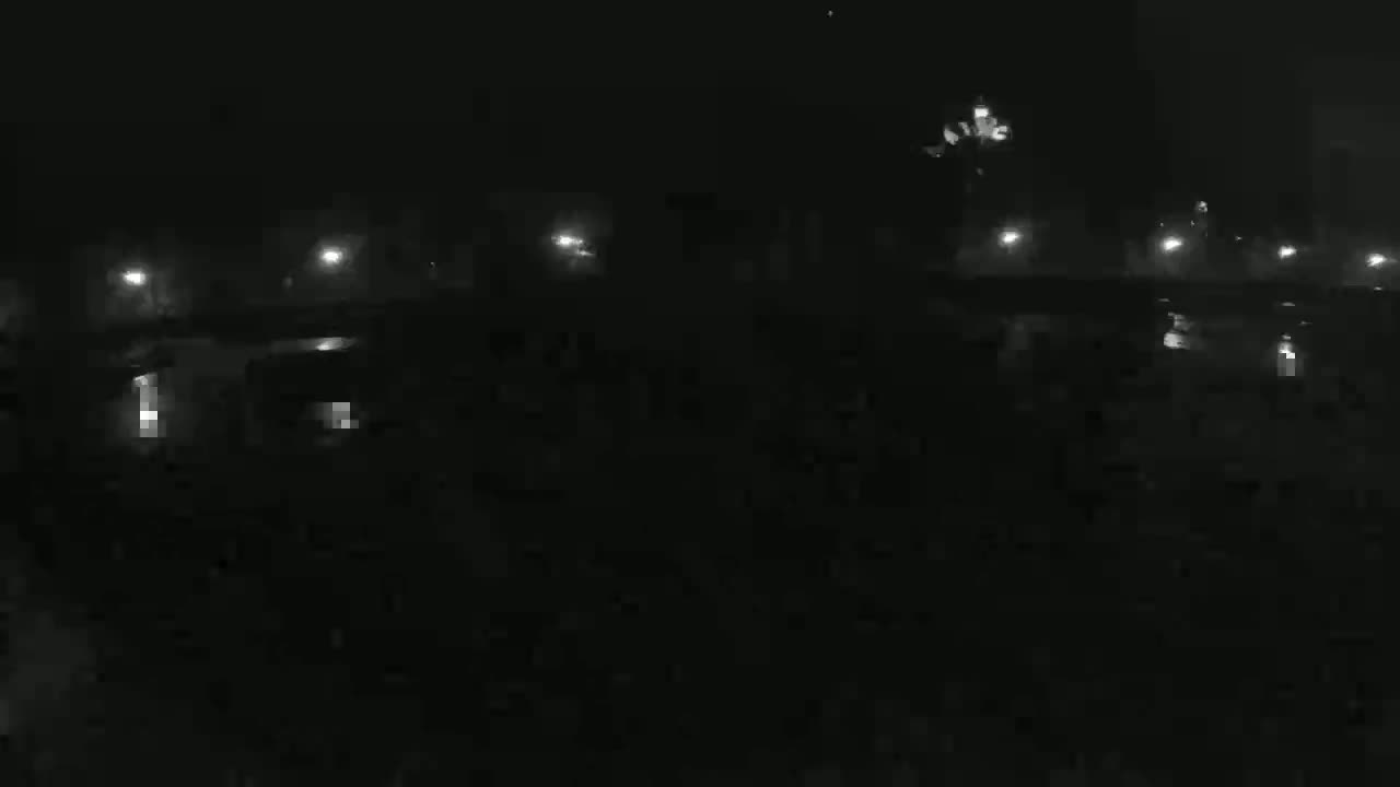A dark, nighttime scene shows a dimly lit roadway with several vehicles and streetlights.