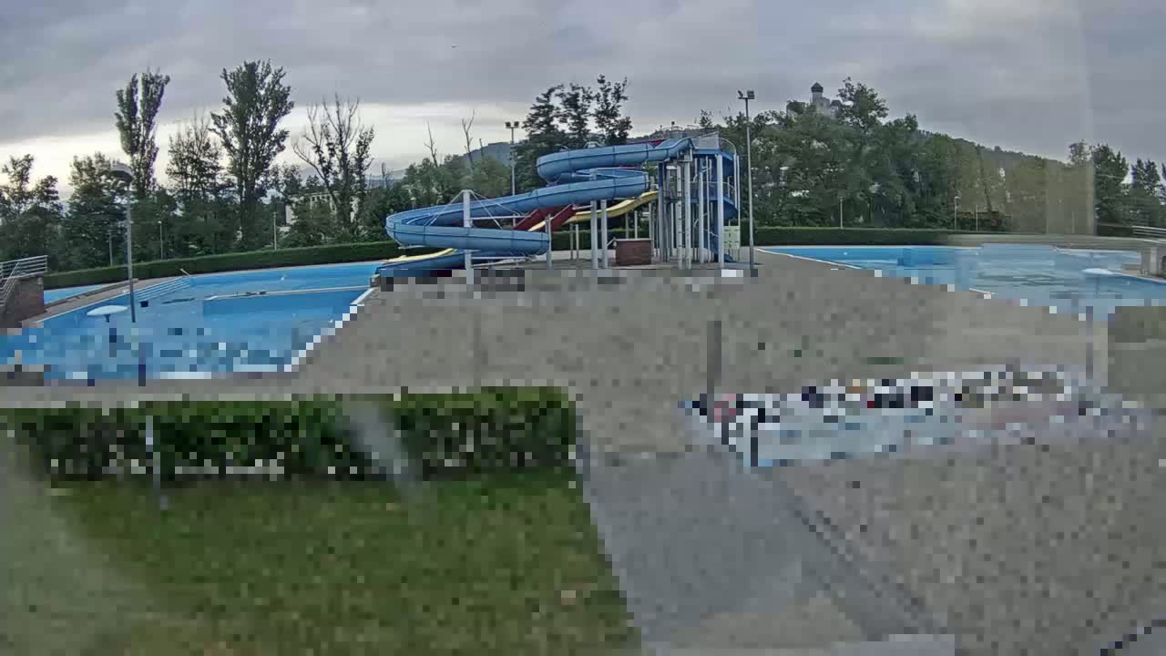 An outdoor swimming pool complex with water slides is visible under an overcast sky.