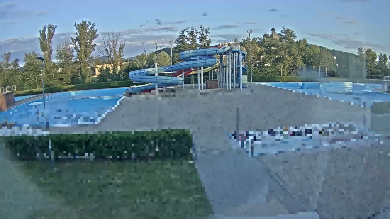 An outdoor swimming pool complex with several water slides is visible under a partly cloudy sky.