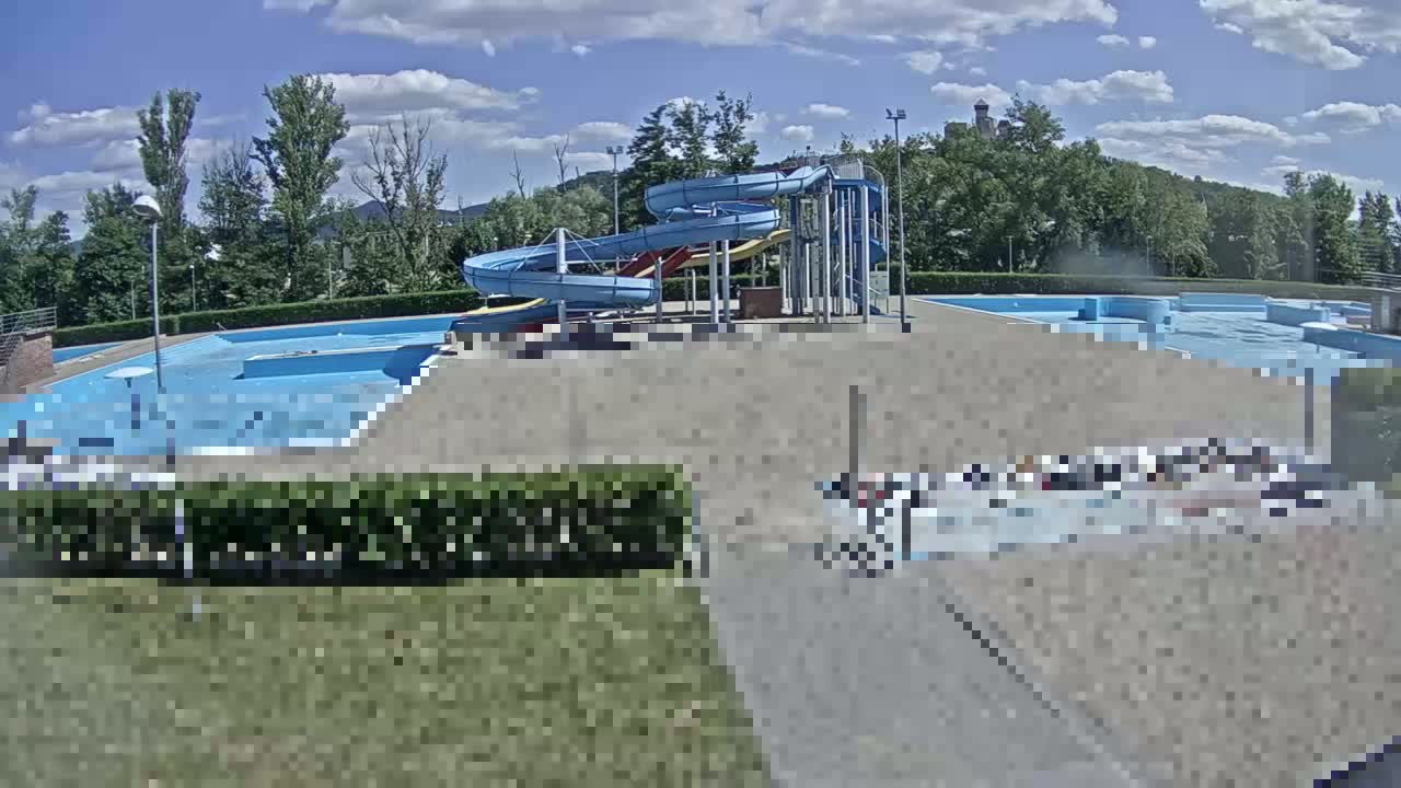 An outdoor swimming pool complex with multiple pools and water slides is visible under a partly cloudy sky.