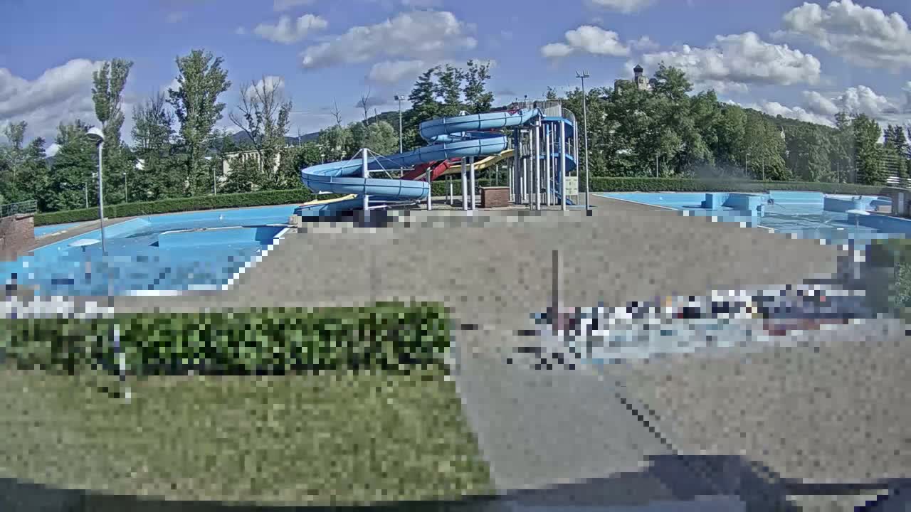 An outdoor swimming pool complex with multiple water slides is shown under a partly cloudy sky.