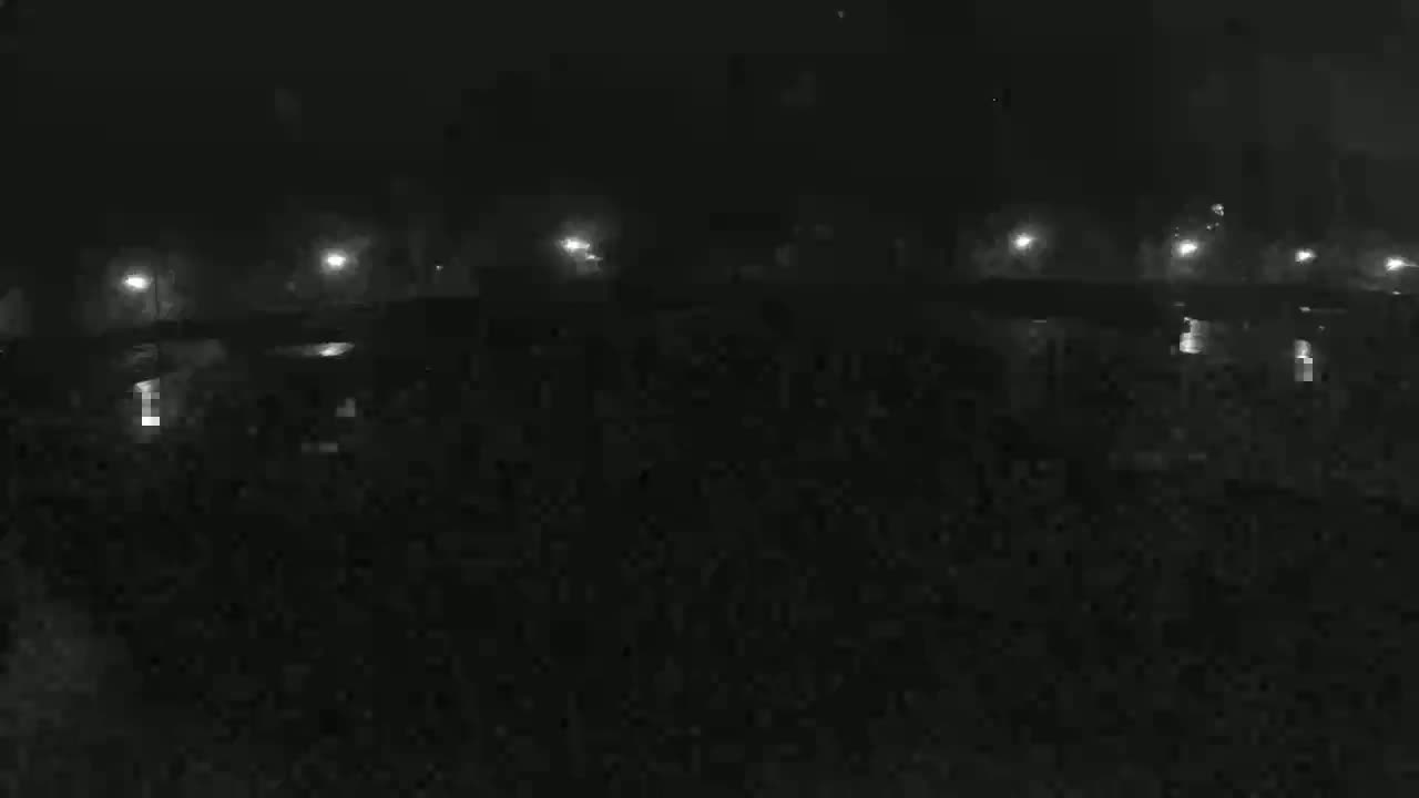 A dimly lit, foggy nighttime scene shows a dark expanse of land with several lights visible in the distance.