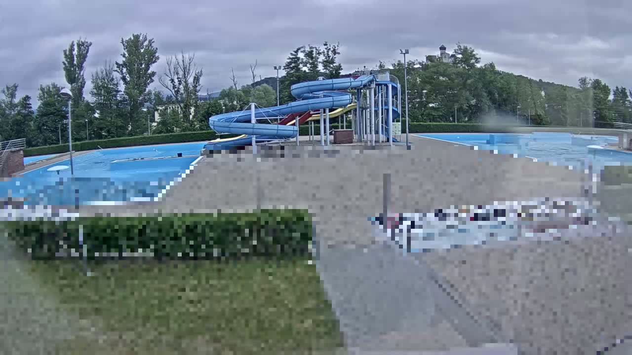 An outdoor swimming pool complex with two water slides is visible under an overcast sky.